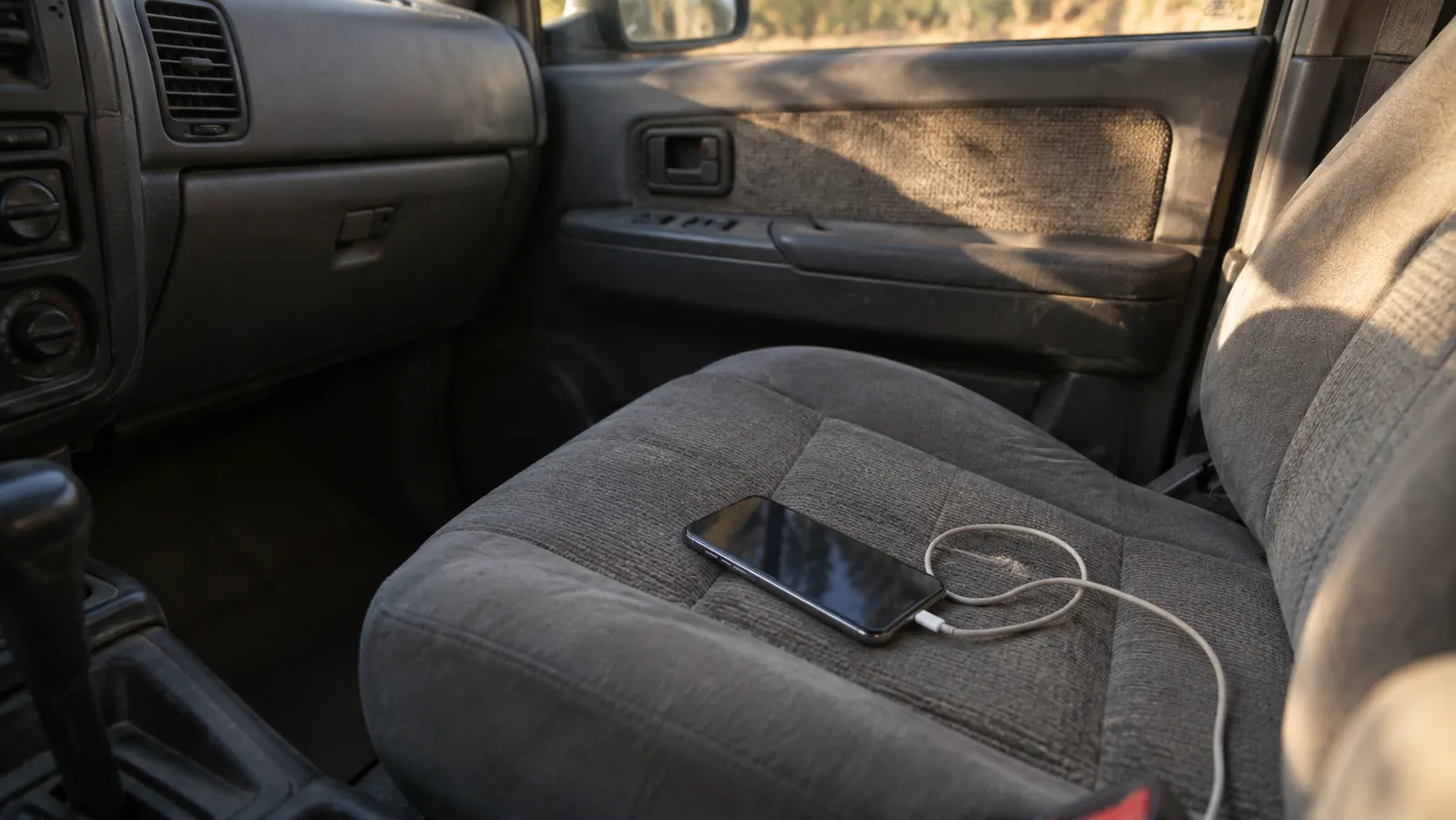 A smartphone lying loose on the passenger seat of an older SUV with a charging cable tangled beside it