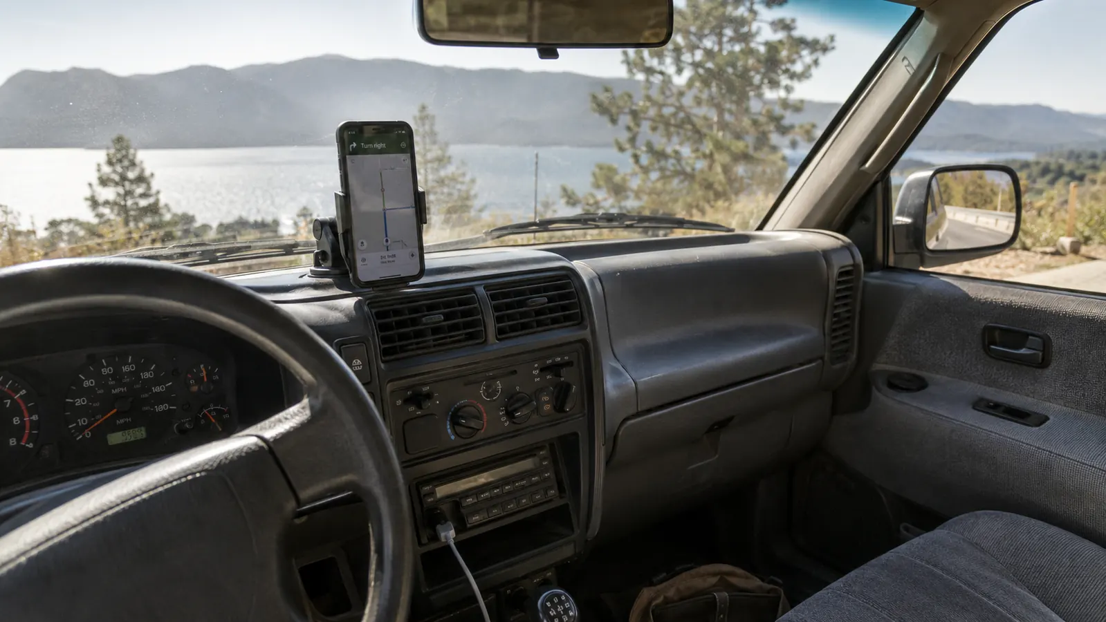 A phone on a dashboard mount inside an older SUV, seen from the driver's seat