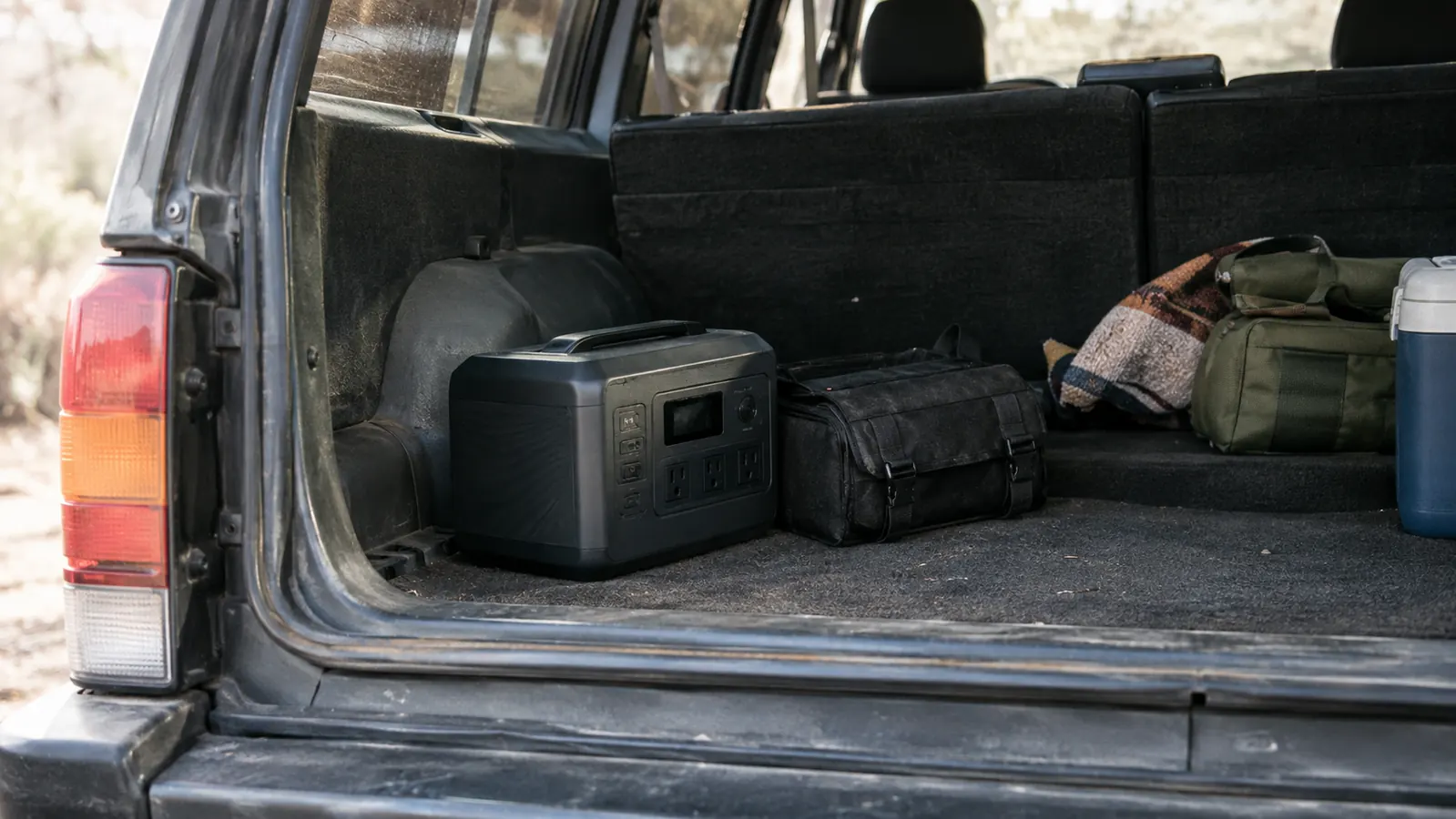 Cargo area of an SUV with a compact battery pack tucked beside a small tool roll