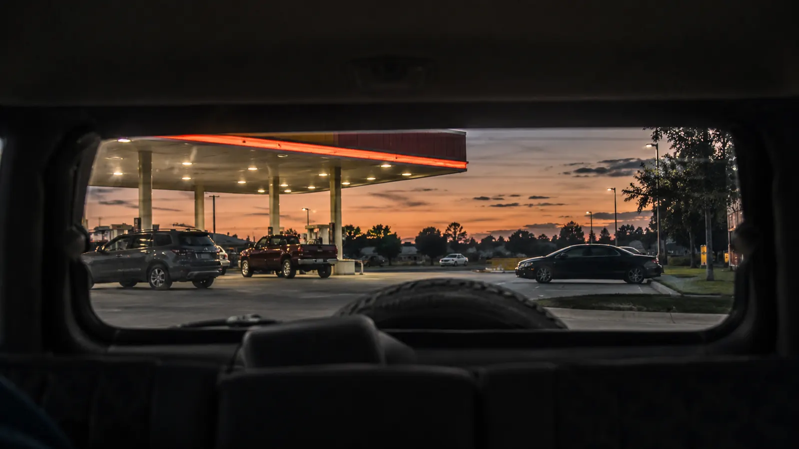 View through an SUV rear window of a gas station parking lot at dusk.